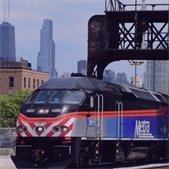 Metra commuter train traveling through an urban area with the Chicago skyline in the background