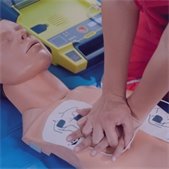 Person performing CPR on a training mannequin with an automated external defibrillator nearby.