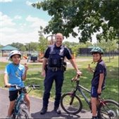 photo of officer with two boys on bikes wearing a helmet and holding up their challenge coin