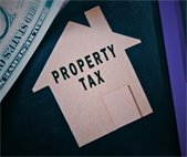 photo of cut out of cardboard shaped house with property tax text and dollar in background