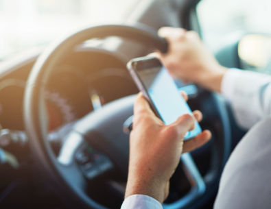 photo of driver with one hand on steering wheel and phone in other hand inside car