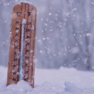 Wooden thermometer showing cold temperatures in falling snow.