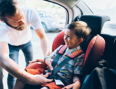 Child in front facing car safety seat getting buckled in by father