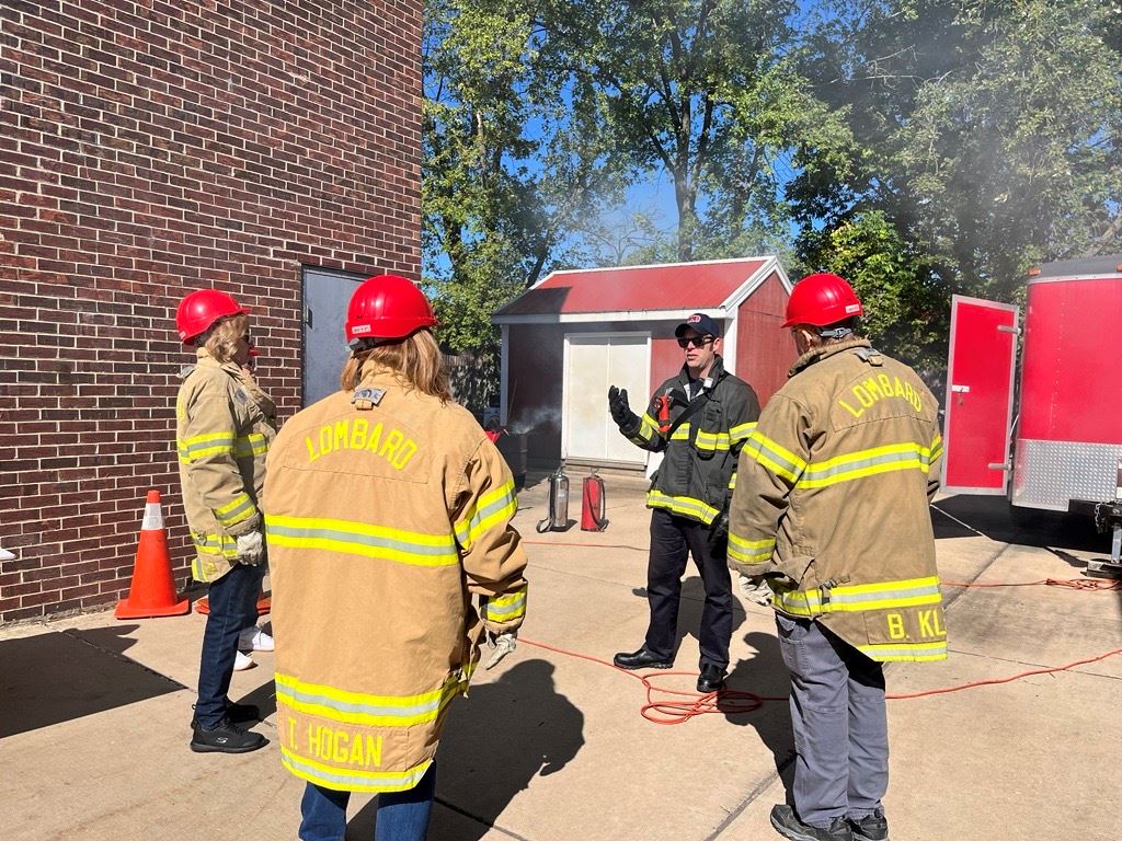 photo of participants wearing firefighter jackets listening to instructor